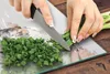 A person is chopping green onions on a glass cutting board, which has a diamond pattern on it. The cutting board is placed on a wooden surface. Produktbild-Vorschau