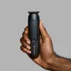 A hand holding a black electric trimmer against a plain gray background. Produktbild-Vorschau