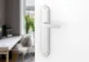 A close-up of a white door handle on a white door, with a blurred background of an office or study. Produktbild-Vorschau