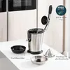 A stainless steel juicer and its accessories are displayed on a white table in a kitchen setting. Produktbild-Vorschau