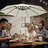 A group of people are enjoying a meal outdoors under a large cantilever umbrella with LED lights. Produktbild-Vorschau