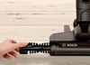 A hand is holding a brush attachment for a vacuum cleaner. Voir les images du produit