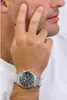 A man's wrist wearing a silver watch with a black face. Anteprima dell’immagine prodotto