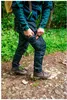 A person is hiking in a forest, reaching into their pants pocket. Produktbild-Vorschau