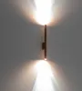 A modern copper wall sconce emitting light upwards and downwards against a gray wall. Náhled obrázku produktu