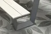 A close-up view of a modern outdoor bench with a light wood seat and a dark gray metal frame, resting on a patterned outdoor rug. Produktbild-Vorschau