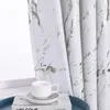 A close-up of a white curtain with silver marble-like patterns, next to a window. A white teacup and saucer sit on a book on a blue tray. Produktbild-Vorschau