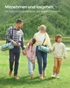 A family walking in a grassy area with trees in the background, carrying rolled-up blankets. Produktbild-Vorschau