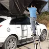 A person is using a ladder to access a rooftop tent on a white car. Voir les images du produit