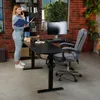 A woman is standing and talking on the phone next to a black adjustable desk in a home office setting. Produktbild-Vorschau