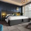 A bedroom scene featuring a large bed with a grey upholstered headboard and frame, bedside tables with integrated lighting, and a large window with curtains. Náhled obrázku produktu