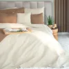 A neatly made bed with a beige quilted bedspread, decorative pillows, and a wooden tray with a book and a cup. Produktbild-Vorschau