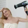A woman is drying her hair with a hairdryer in a bathroom. Produktbild-Vorschau