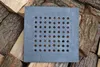 A square cast iron grate with many small holes is placed on a pile of chopped wood. Anteprima dell’immagine prodotto
