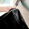 A hand holding a black silicone baking mat under running water from a faucet. Voir les images du produit