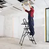 A person is standing on a ladder and working on a ceiling light fixture. Anteprima dell’immagine prodotto