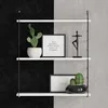 A white three-tiered shelf unit mounted on a wall with a black and gray textured background. The shelves display decorative items including potted cacti, framed pictures with text, and a figurine. Anteprima dell’immagine prodotto