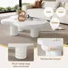 A white, irregularly shaped coffee table with thick legs is shown in a living room setting with a sofa in the background. Insets highlight the table's features. Voir les images du produit