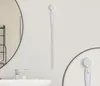 A white cleaning brush for sink drains is mounted on a white wall next to a bathroom mirror and sink. Produktbild-Vorschau