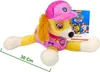 A plush toy of Skye from Paw Patrol lying down, with its packaging in the background. Produktbild-Vorschau