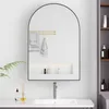 A bathroom vanity with a sink, faucet, and a large arched mirror above it. The mirror reflects towels and a shelf with toiletries. A plant is visible to the left. Produktbild-Vorschau
