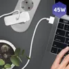 A laptop being charged by a power adapter connected to a wall socket, with a plant in a pot in the foreground. Produktbild-Vorschau