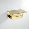 A gold-colored toilet paper holder with a small shelf, mounted on a white wall. Anteprima dell’immagine prodotto