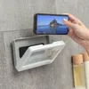 A hand is holding a smartphone in front of a waterproof phone case mounted on a tiled wall in a bathroom. Podgląd zdjęcia produktu