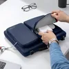 A person is placing an item into a blue laptop bag on a white desk. Produktbild-Vorschau