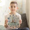 A young boy is holding a round wall clock with a sailing ship painted on it. Produktbild-Vorschau
