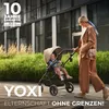 A woman pushing a baby stroller on a paved walkway next to a grassy area and a modern building. Anteprima dell’immagine prodotto