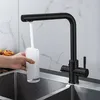 A black faucet is filling a glass with water over a sink. Produktbild-Vorschau