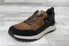 A single brown and black sneaker is shown from a side angle on a light-colored wooden floor. Voir les images du produit