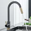A modern kitchen faucet with a pull-down sprayer is shown in use, with water flowing into a sink. Cucumbers and other kitchen items are visible in the background. Náhľad obrázku produktu