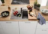 A kitchen counter with a sink, cutting board, vegetables, and cooking utensils. Produktbild-Vorschau