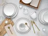 A flat lay of a white dinnerware set with gold accents, arranged on a light gray surface with some decorative elements. Náhľad obrázku produktu