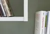 A close-up view of books on a white shelf against a gray wall. Produktbild-Vorschau