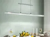 A modern dining table setting with a long, linear pendant light fixture hanging above. Produktbild-Vorschau