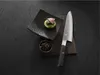 A chef's knife is placed next to a small dish of food and a bowl of dark grains on a dark textured surface. Produktbild-Vorschau