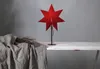 A red star-shaped lamp sits on a white table next to a grey cloth and some dried branches. Podgląd zdjęcia produktu