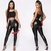 Frau trägt glänzende schwarze Leggings aus Kunstleder und ein schwarzes Crop Top, von vorne und hinten gezeigt, mit roten Pfeilen, die die Dehnbarkeit anzeigen Produktbild-Vorschau