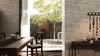A dining room with a wooden table and chairs, looking out onto a courtyard with a tree and stone walls. Produktbild-Vorschau