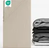 A close-up of a beige fitted sheet with a stack of folded sheets in various shades of gray and black on the right side. Produktbild-Vorschau