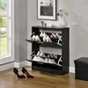 A black shoe cabinet with two flip-out drawers filled with shoes, placed next to a window and a black storage ottoman. Náhled obrázku produktu