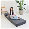 A young woman is sitting on a folded mattress in a room with a plant and a chair. Podgląd zdjęcia produktu