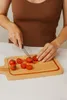 A person is cutting tomatoes on a wooden cutting board. Podgląd zdjęcia produktu