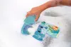 A child's hand is playing with bath toys in a foamy bathtub. Produktbild-Vorschau