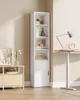 A tall, narrow white bookshelf with a door on the bottom section and open shelves above, placed in a room with a light beige wall. Náhled obrázku produktu