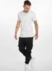 A man wearing a white t-shirt and black cargo pants stands against a white background. Anteprima dell’immagine prodotto