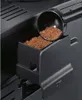 A close-up view of a coffee scoop filled with coffee grounds being poured into a coffee machine's grounds compartment. Produktbild-Vorschau